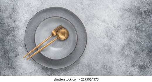 Gray Ceramic Plates With Gold Cutlery. Gray Stone Grunge Background. Top View, Banner. Minimal Table Setting.