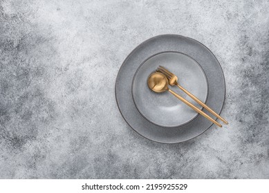 Gray Ceramic Plates With Golden Cutlery. Gray Stone Grunge Background. Minimal Table Setting. View From Above