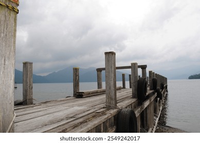 Gray Cloudy Day on Lake Chuzenji at the Base of Mount Nantai in Nikko Japan Asia with Long Wooden Dock Along Rocky Sandy Beach Shoreline with Mountains in the Distance and Swan Pedal Boats - Powered by Shutterstock