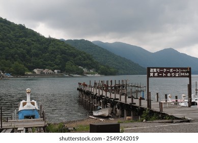 Gray Cloudy Day on Lake Chuzenji at the Base of Mount Nantai in Nikko Japan Asia with Long Wooden Dock Along Rocky Sandy Beach Shoreline with Mountains in the Distance and Swan Pedal Boats - Powered by Shutterstock