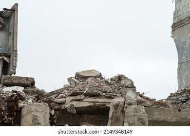 Gray debris of the building in the form of large concrete piles, slabs, beams with remnants of a brick wall against a gray sky. Background.