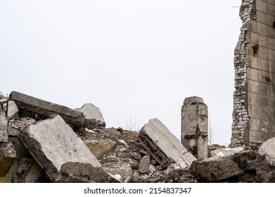 Gray debris of the building in the form of large concrete piles, slabs, beams with remnants of a brick wall against a gray sky. Background.
