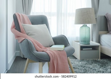 Gray easy armchair with pink scarf, pillow and book next to bed in the bedroom