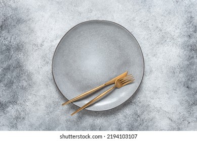 Gray Empty Plate With Golden Cutlery. Gray Stone Background. Top View, Flat Lay. Minimal Table Setting.