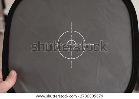A gray fabric target panel with a white crosshair marking is held indoors.