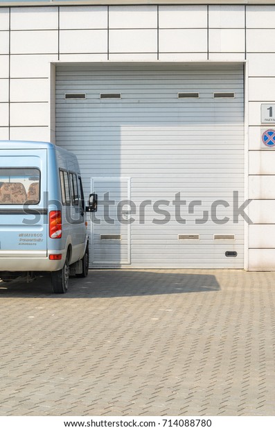 Gray\
garage door and a parked minibus. Large automatic up and over\
garage door with inclusion of smaller personal\
door.