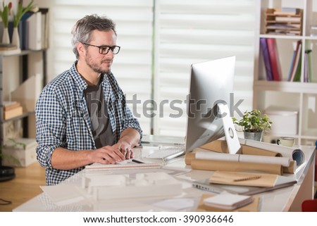 Gray haired architect wearing beard, sitting at office and working on a building project