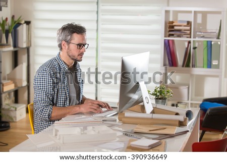 Gray haired architect wearing beard, sitting at office and working on a building project