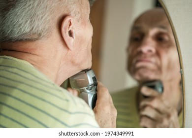 Gray Haired Senior Man Looking In Mirror And Shaving With Electric Razor. Daily Body Care Concept.