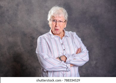 gray hairy elderly woman with crossed arms looking angry in front of gray background
