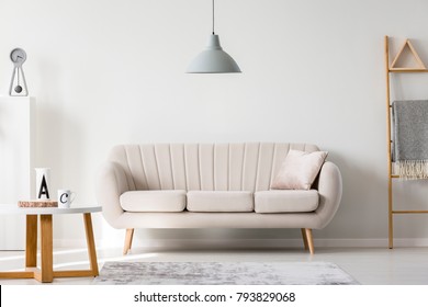 Gray lamp above beige couch in sophisticated living room interior with ladder and wooden round table