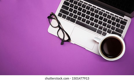 gray laptop with a cup of coffee and glasses on purple background table, working place at home or in the office - Powered by Shutterstock