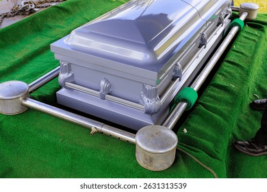 Gray metal coffin rests in grassy area of cemetery somber atmosphere solemnity during funeral preparation