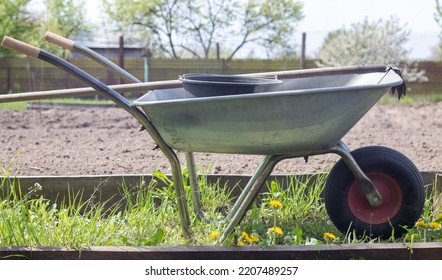 Gray metal garden wheelbarrow with two handles and one wheel. The wheelbarrow is in the garden or garden. Gardener's wheelbarrow in the backyard. Garden cleaning
