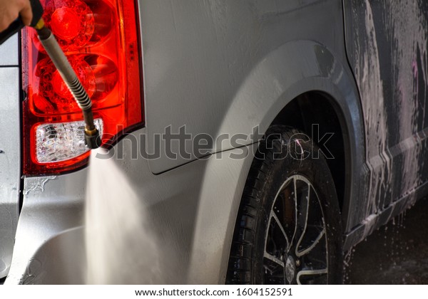 gray minivan back
right side black tire with red rear lights being power washed with
a spray gun at a car wash