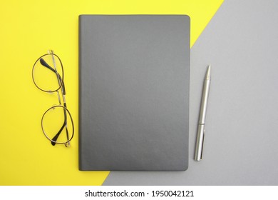 A gray notepad, pen, and stylish glasses are placed on a gray-yellow background.Things for businessmen, education, technology concept, top view.The colors of 2021 are gray and yellow.Copyspace