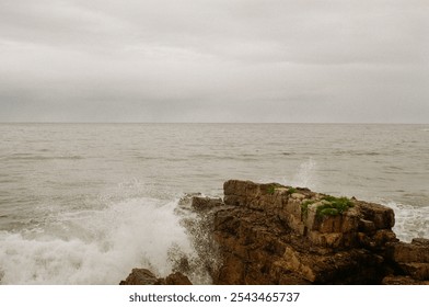 A gray, overcast sky above a rocky shore with ocean waves crashing. - Powered by Shutterstock