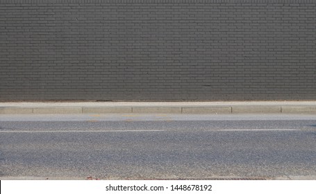 Gray Painted Brick Wall With Concrete Sidewalk And Asphalt Road In Front. Background For Copy Space.