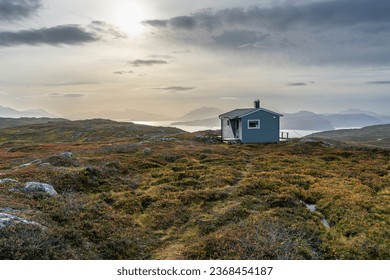 gray painted hut on Norwegian mountain, with view of fjord and coastal landscape of Norway. Ski lodge near Tromsø in colorful autumn. rough rocky landscape with colorful plants.