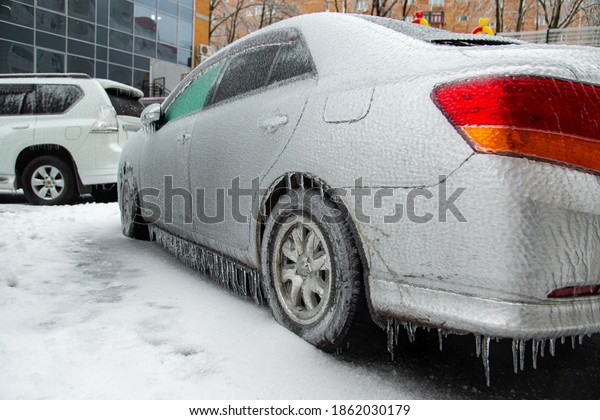 The gray passenger car\
was covered with a thick crust of ice after the wet rain in the\
city in winter.