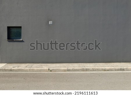 Gray plaster wall with a window and small air inlet. Concrete sidewalk and asphalt road in front. Background for copy space