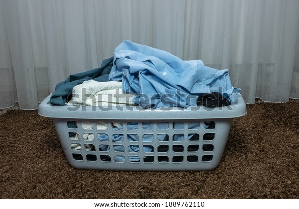 Gray plastic basket with dirty laundry in the\
bedroom on the carpet