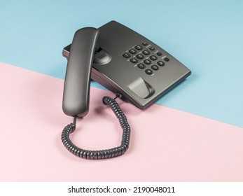 Gray push-button phone with the handset off on a pink and blue background. The concept of telephone communication.