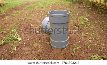 A Gray pvc pipe fitting elbow joint standing on soil outdoors in garden yard, plumbing drainage connector on ground with grass and dirt background.