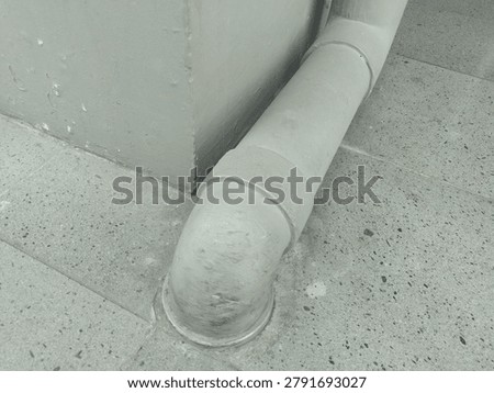 A gray PVC pipe is installed in the corner between the ceramic floor and the wall. It uses 90-degree elbows on both ends, connecting the vertical pipe to the wall pipe.