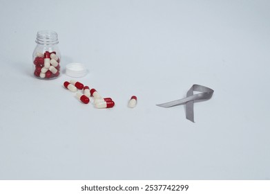 Gray ribbon symbol and some medicine capsules isolated on white background, symbol to commemorate the month of awareness for diabetes and cancer sufferers. Health and medicine concept - Powered by Shutterstock