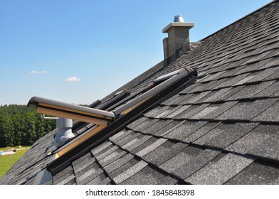 A Gray Roof Covered With Dimensional Architectural Asphalt Shingles With An Attic Skylight, Ventilation Pipe, Air Duct And Chimney. A Close-up On An Open Attic Skylight.   