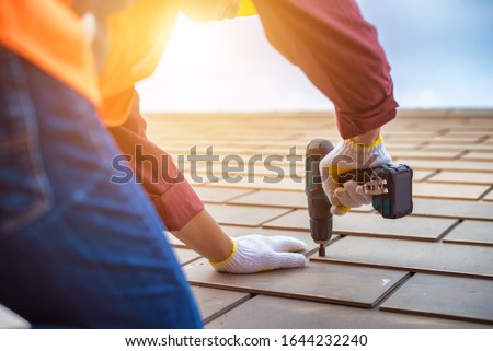 Gray roof - Repair and Replace the House Roof with Handyman with Tools and Pprotective equipment. Stand on the Roof with the Ssky Background.