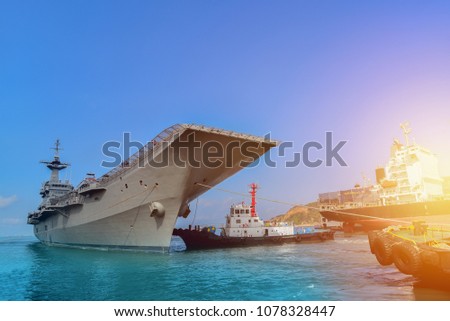 Gray ship museum aircraft carrier for a planes and Tug boat assistance to wharf in shipyard for being renovated on blue sky background