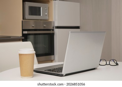 Gray Silver Laptop, Mobile Phone ,  Paper Coffee Cup Standing On White Wooden Table With Kitchen Background. No People.