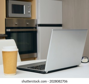 Gray Silver Laptop, Mobile Phone ,  Paper Coffee Cup Standing On White Wooden Table With Kitchen Background. No People.