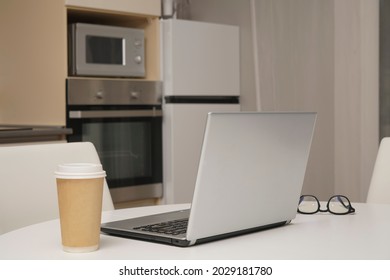 Gray Silver Laptop, Mobile Phone ,  Paper Coffee Cup Standing On White Wooden Table With Kitchen Background. No People.