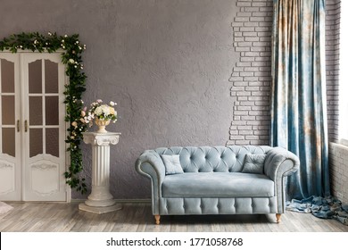 Gray sofa chester on a background of gray wall in classic livingroom with column, vintage doors and flowers