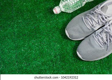 Gray Sports Running Shoes and bottle of water on green grass.  Sport and relax concept.