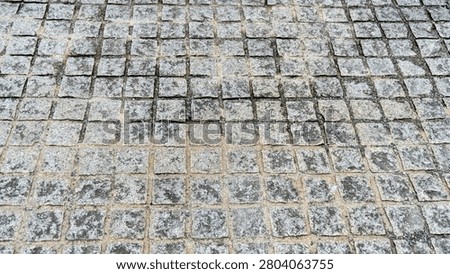 Gray square stone sett paving in a grid pattern, an outdoor stone ground texture.