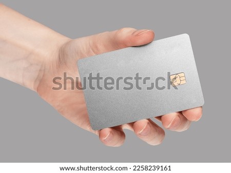 Gray stylish minimalistic bank credit card mockup in hand on gray background. Blank clean silver gray debit plastic bankcard with chip. High quality photo