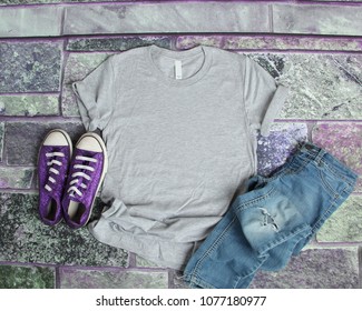 Gray T Shirt Mockup Flat Lay On Purple Brick Background With Purple Shoes And Ripped Jeans