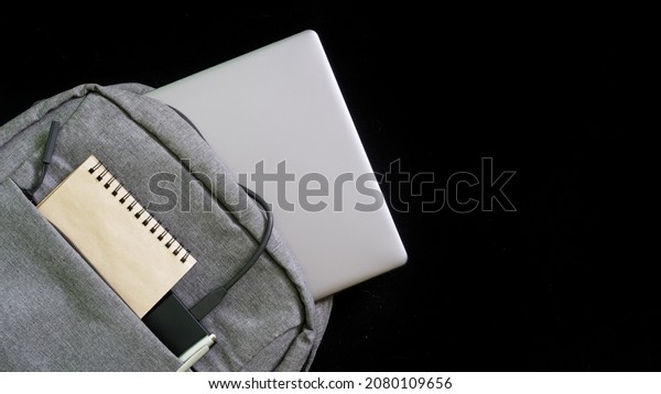 Gray textile backpack with laptop, notepad and\
external ssd or power bank on a black background. Backpack concept\
for high school student or manager. Free space for an inscription.\
Close-up