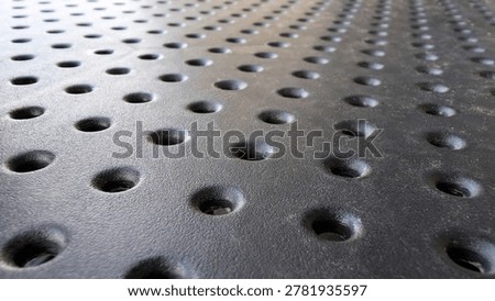 Gray textured surface featuring a grid of small, round indentations creating a uniform perforated pattern, useful as an abstract background for technology, industrial, or design contexts