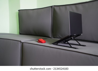 A Gray Thin Laptop On A Stand And A Red Computer Mouse On A Gray Loft-style Sofa. The Concept Of Remote Work And Internet Access From Home. Nobody. Without People. Close-up