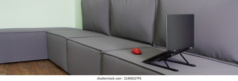 Gray Thin Laptop On A Stand And A Red Computer Mouse Stand On A Large Gray Loft Sofa. The Concept Of Remote Work And Internet Access From Home. Nobody. Without People. Web Banner. Close-up