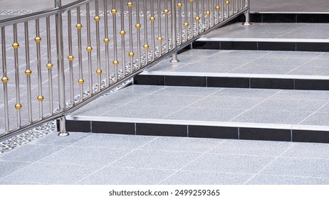 Gray tile steps of elevated walkway with flat path for wheelchair and stainless steel railing on the ramp area in entryway of outdoors public restroom, perspective side view