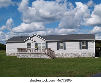 Gray trailer home with stone foundation or skirting and shutters in front of a beautiful sky.