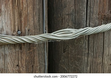 Gray Twisted Metal Wire Pulls Together Two Brown Wooden Pillars In The Street