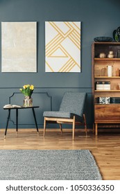 Gray, Upholstered Chair Next To An Elegant, Wooden Bookcase In A Reading Corner Of A Dark Living Room Interior With Molding