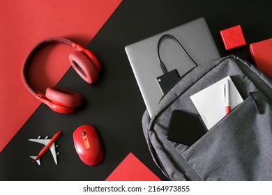 Gray urban backpack with a laptop, ssd drive, phone, notepad and pen on black and red next to mouse, headphones and toy plane. Gadgets and luggage of students, IT people and journalists. Close-up - Shutterstock ID 2164973855